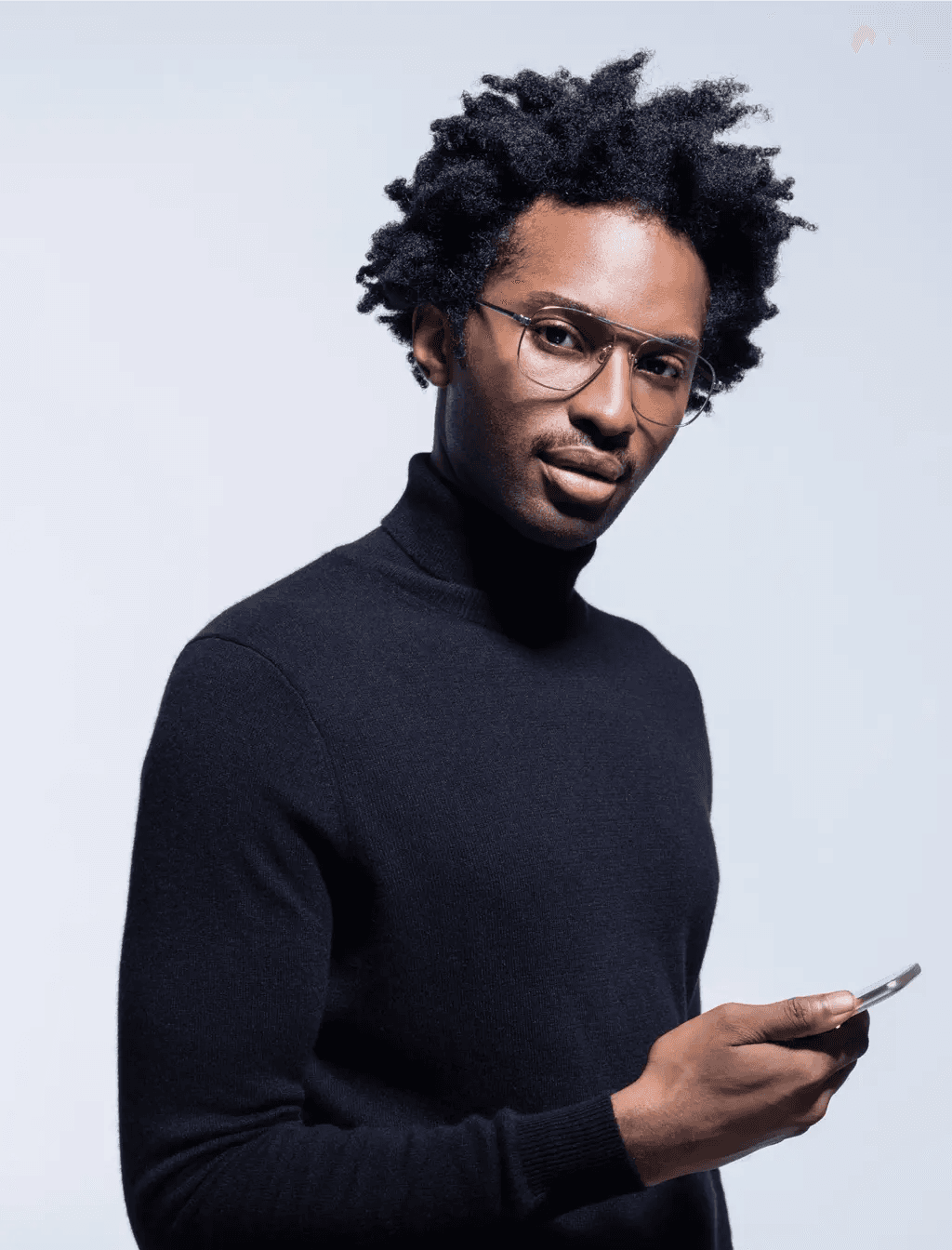 A man wearing glasses and a black turtleneck is holding a cell phone.