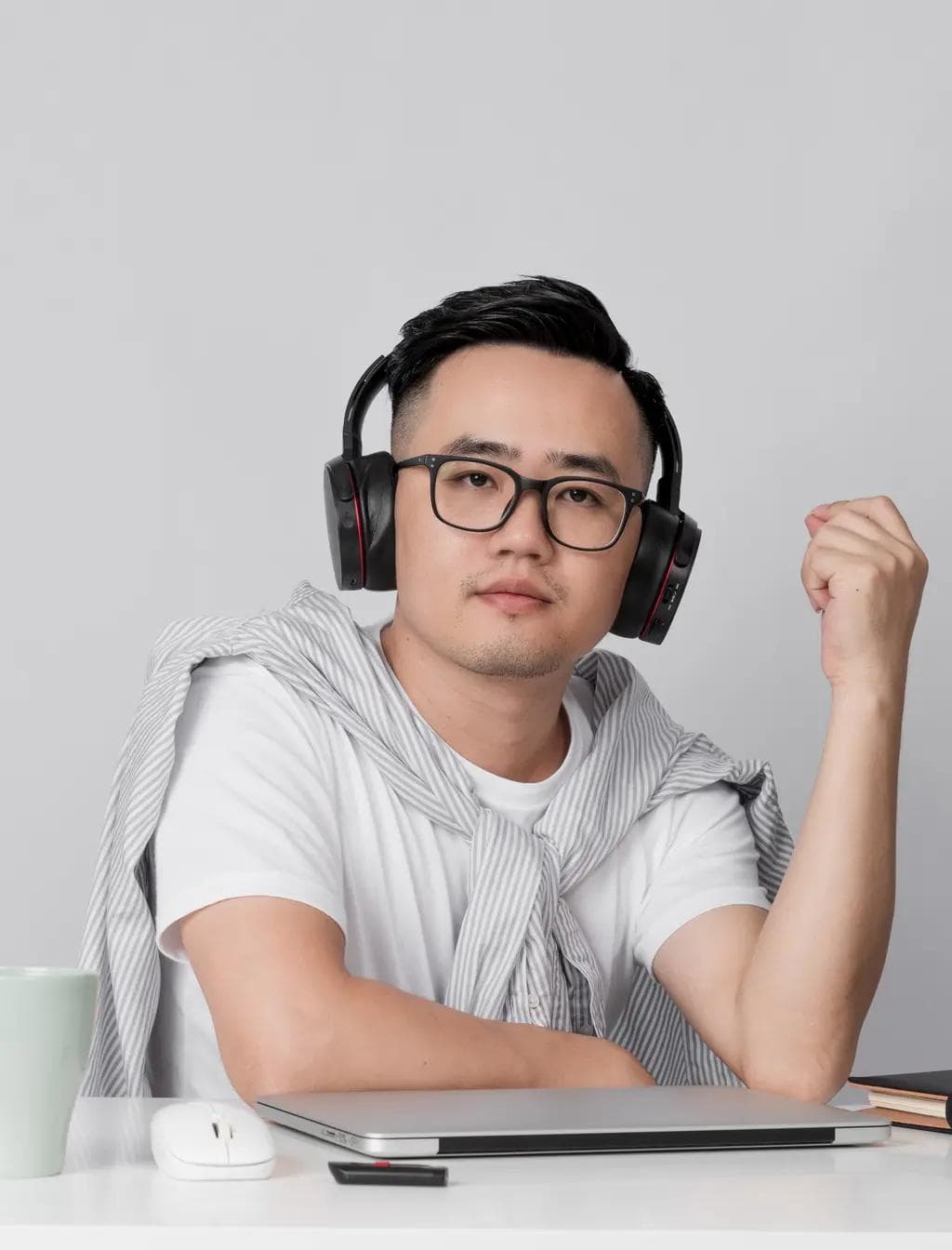 A man wearing headphones and glasses is sitting at a desk with a laptop.