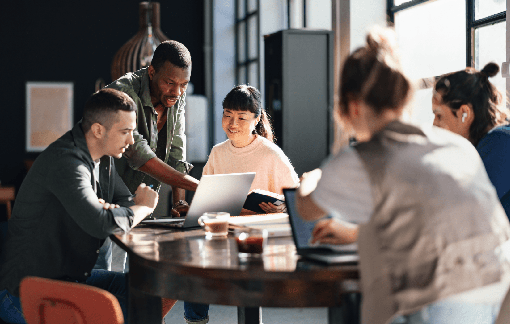 Image of a group of people sitting at a round table looking at laptops.