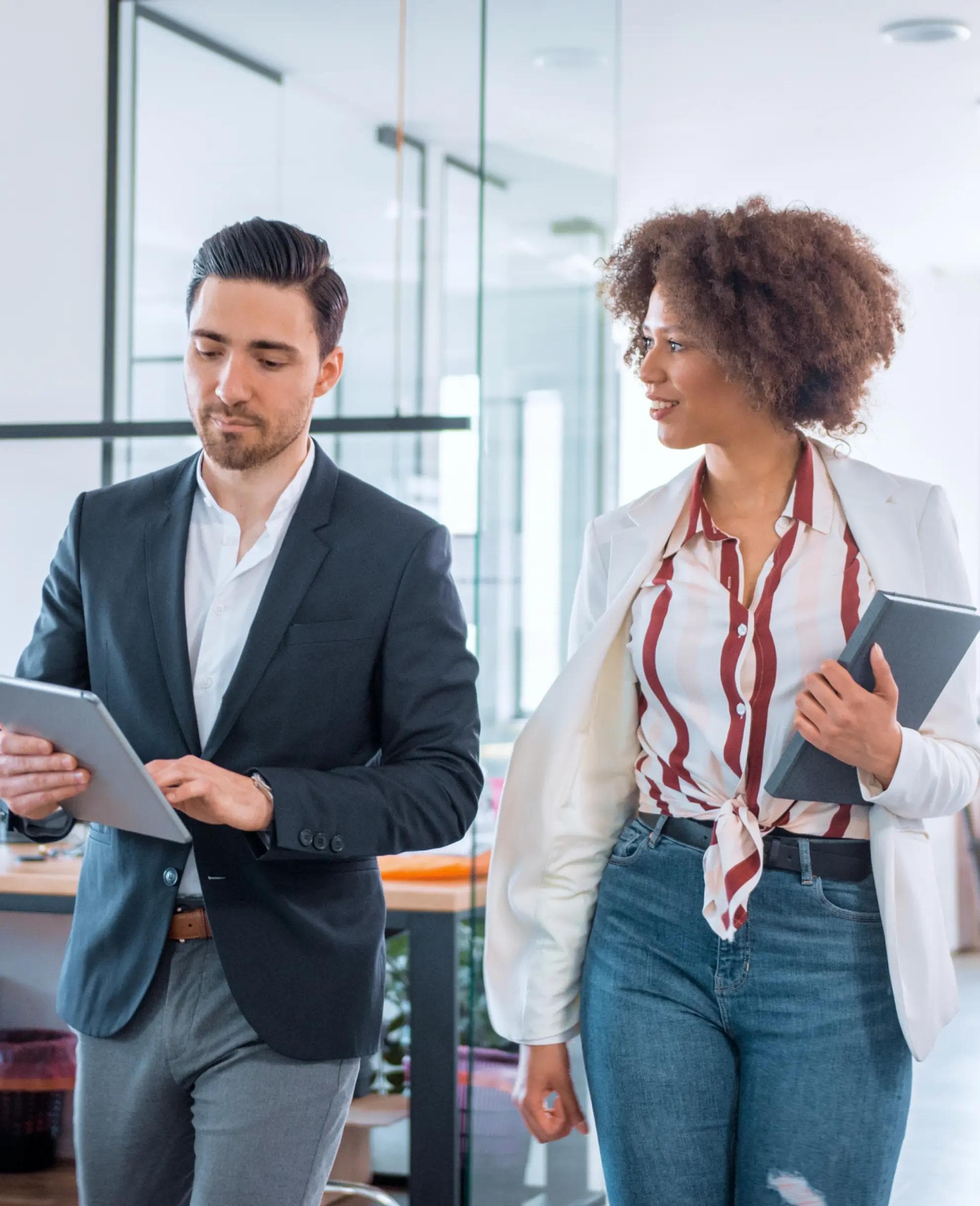 Two people walking through office with tablets in hand.