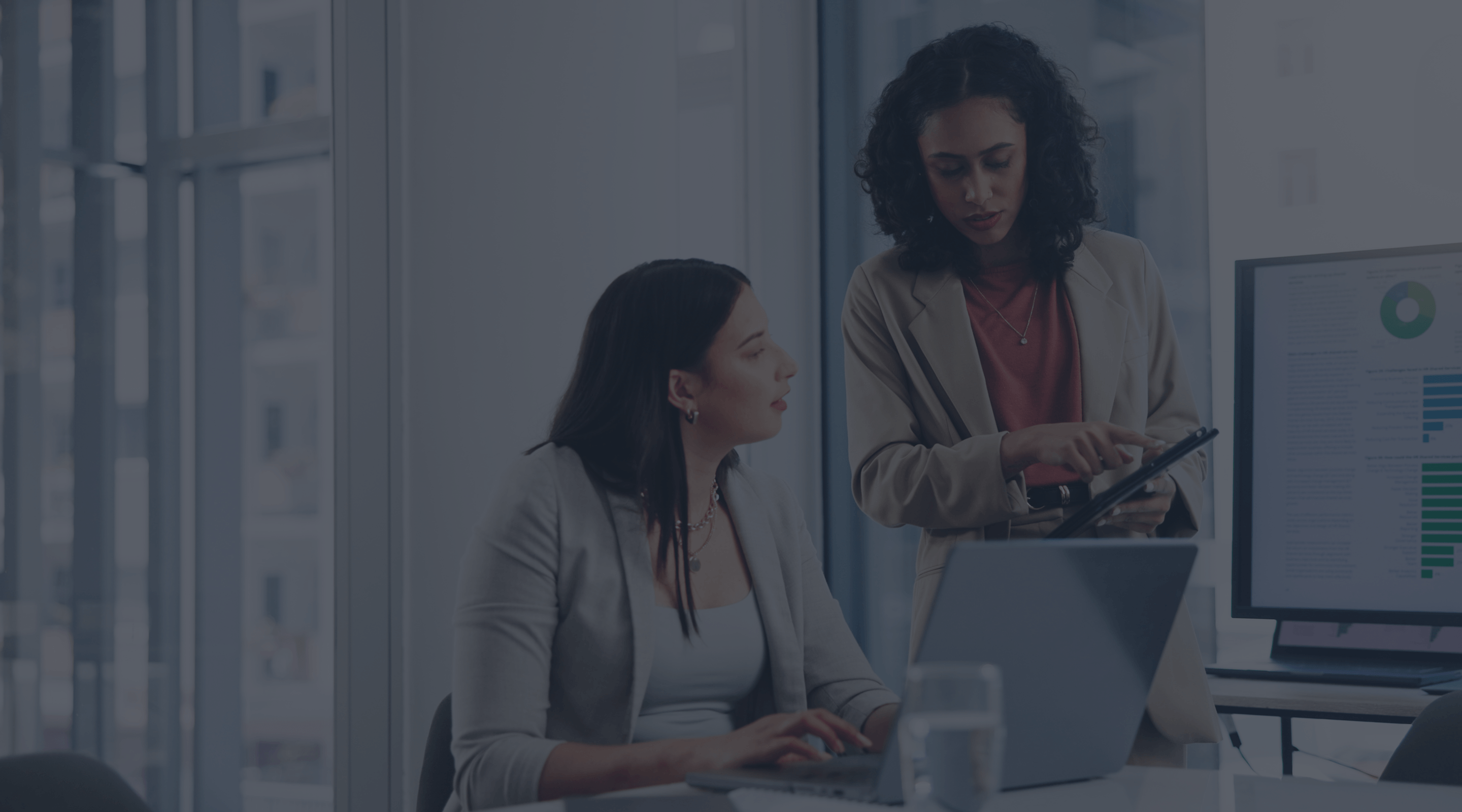 Image of two women viewing a tablet with a laptop.